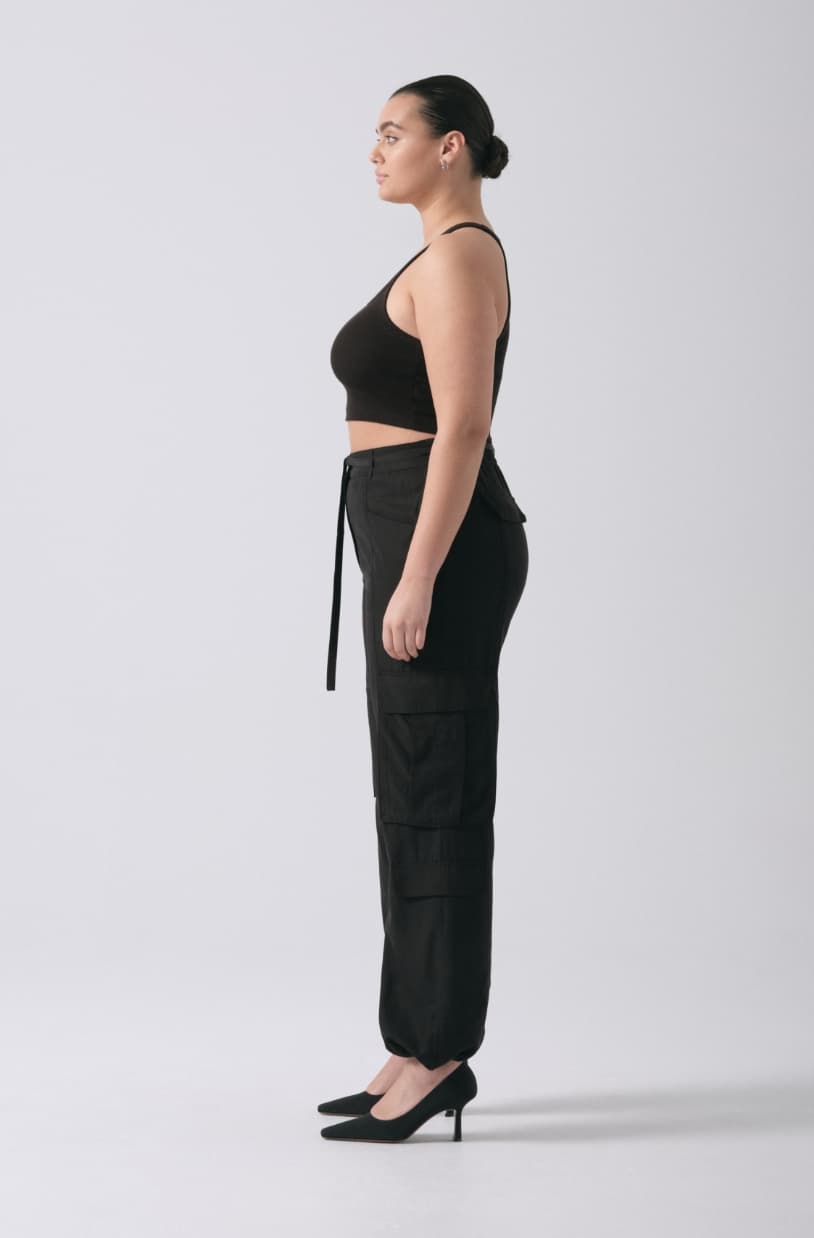 Une mannequin porte un pantalon cargo noir avec une cami noire.