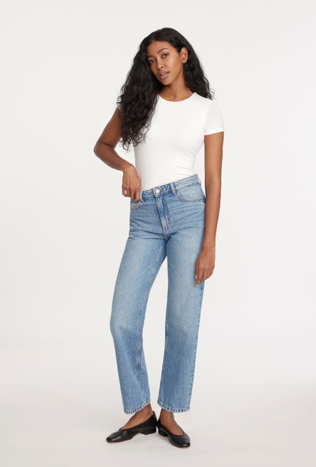 Model is wearing a white shirt and wide leg jeans.