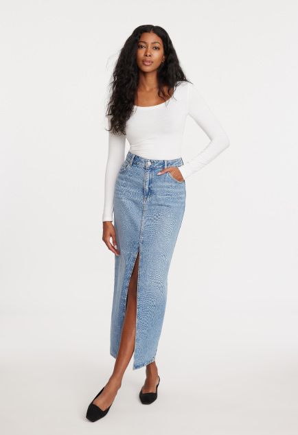 Model is wearing a white long sleeve shirt and a blue denim maxi skirt.