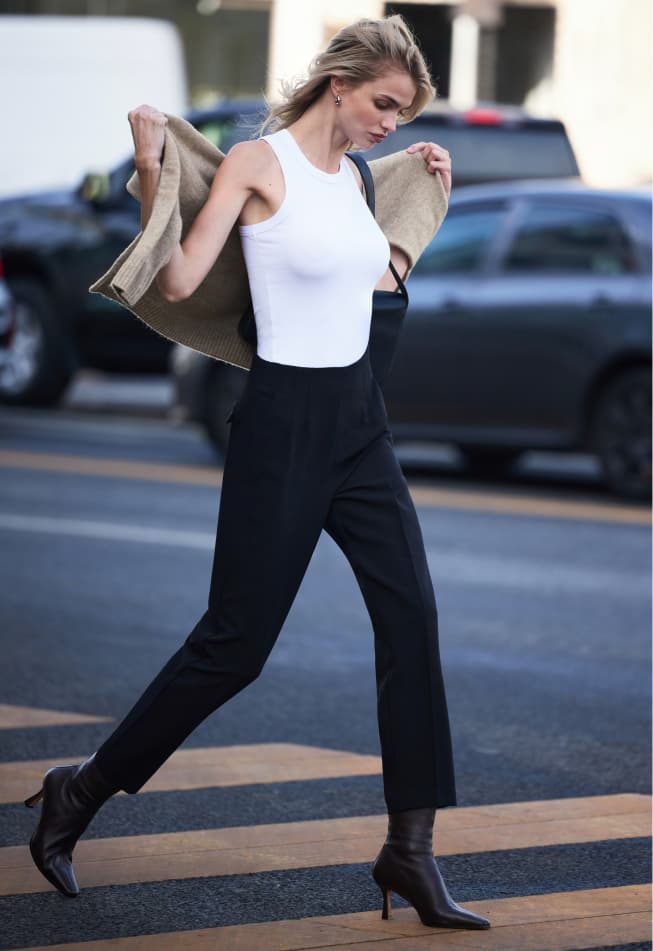 Model is wearing a brown tweed blazer over a white mock neck top and indigo bootcut jeans.