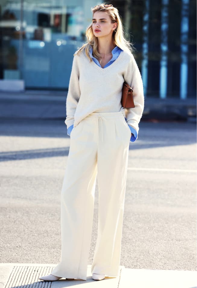 Model is wearing a black faux leather jacket over a white tank top, blue wide leg jeans, and a black faux leather belt.