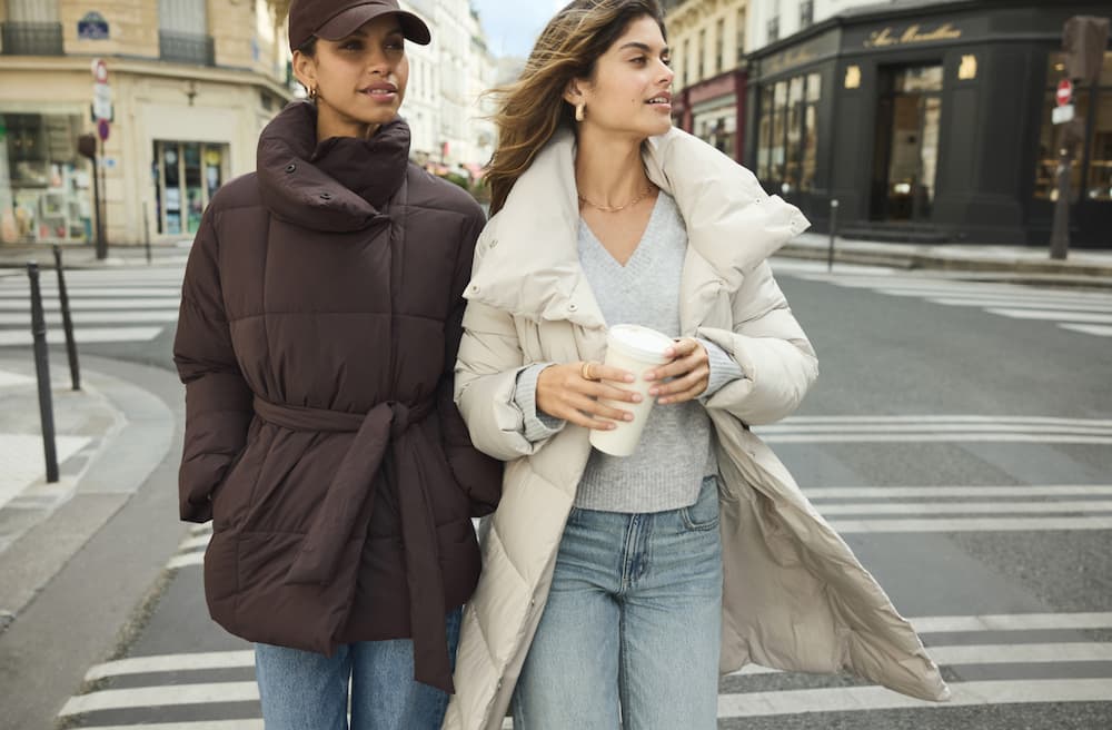 Les mannequins traversent la rue vêtues d'un manteau matelassé brun et d'un manteau matelassé blanc.