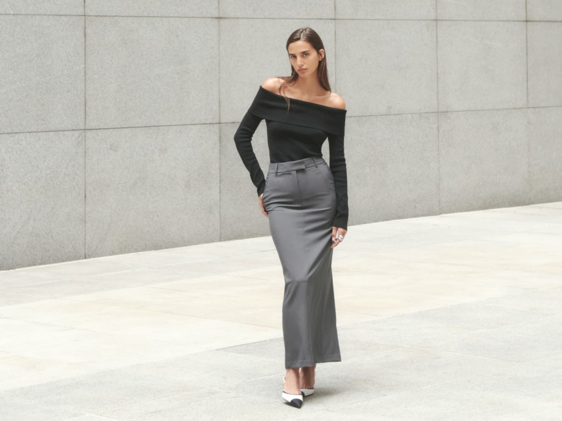 A model wears a grey maxi skirt with a black off-the-shoulder long sleeve top.