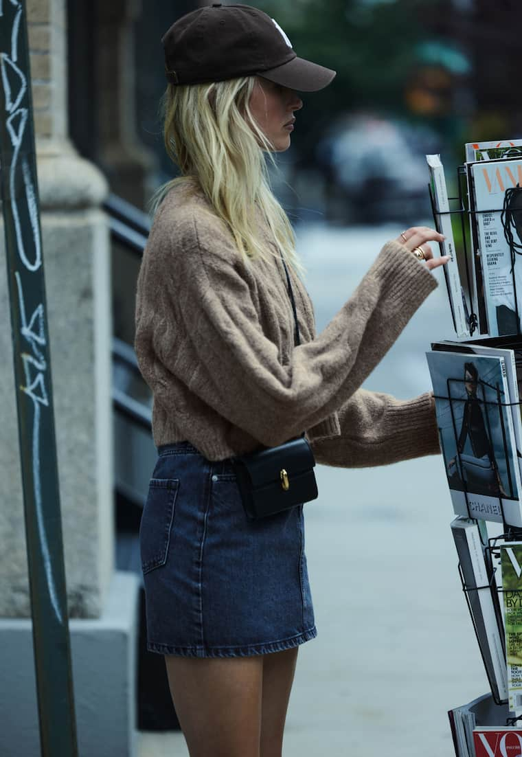 Model is wearing a brown knit sweater and a blue denim mini skirt.