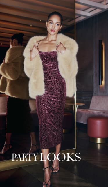 Model is wearing a beige faux fur jacket over a burgundy maxi dress with a velvet floral print.