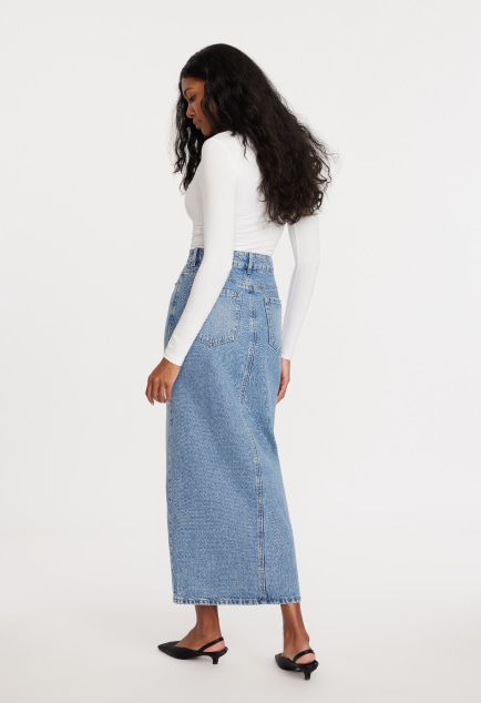Model is wearing a white long sleeve shirt and a blue denim maxi skirt.