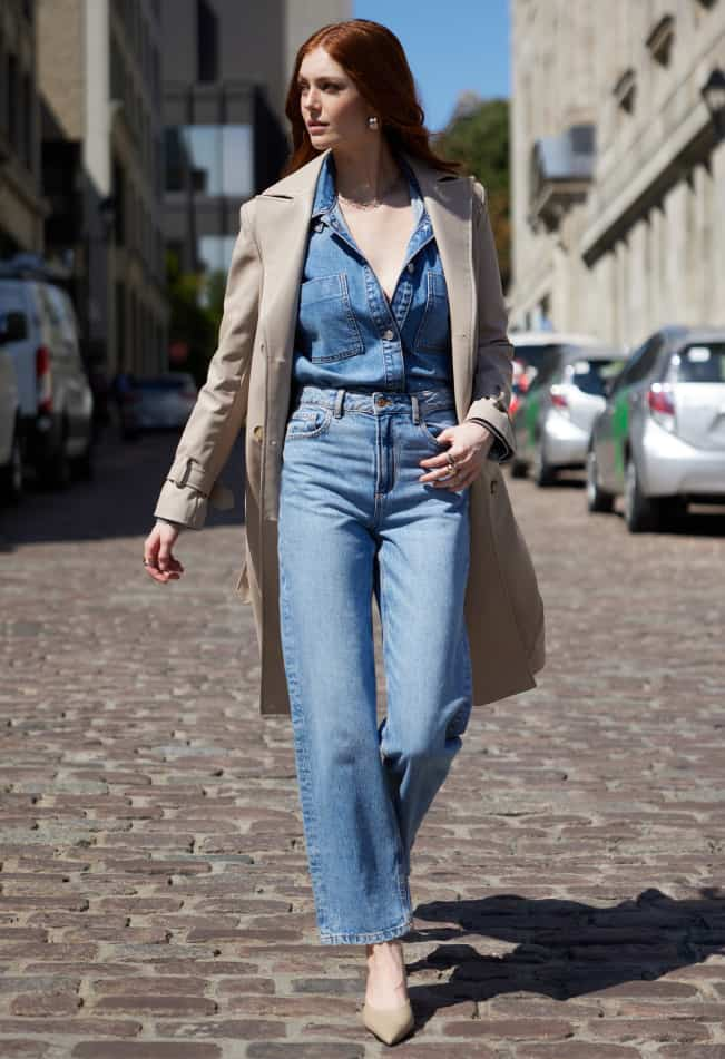 La mannequin porte un trench beige sur une chemise bleue en denim et un jean bleu à jambe droite.