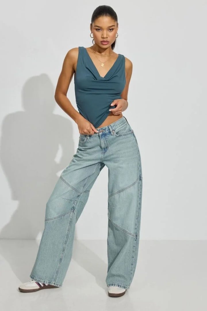 Model wears a black apron back top and light wash baggy jeans with black sneakers.