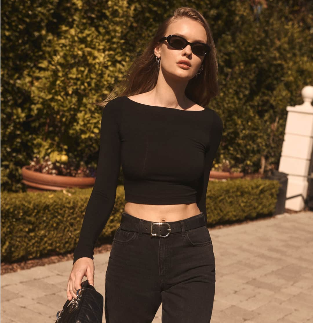 A model wears a one shoulder black sleeveless top with blue jeans.