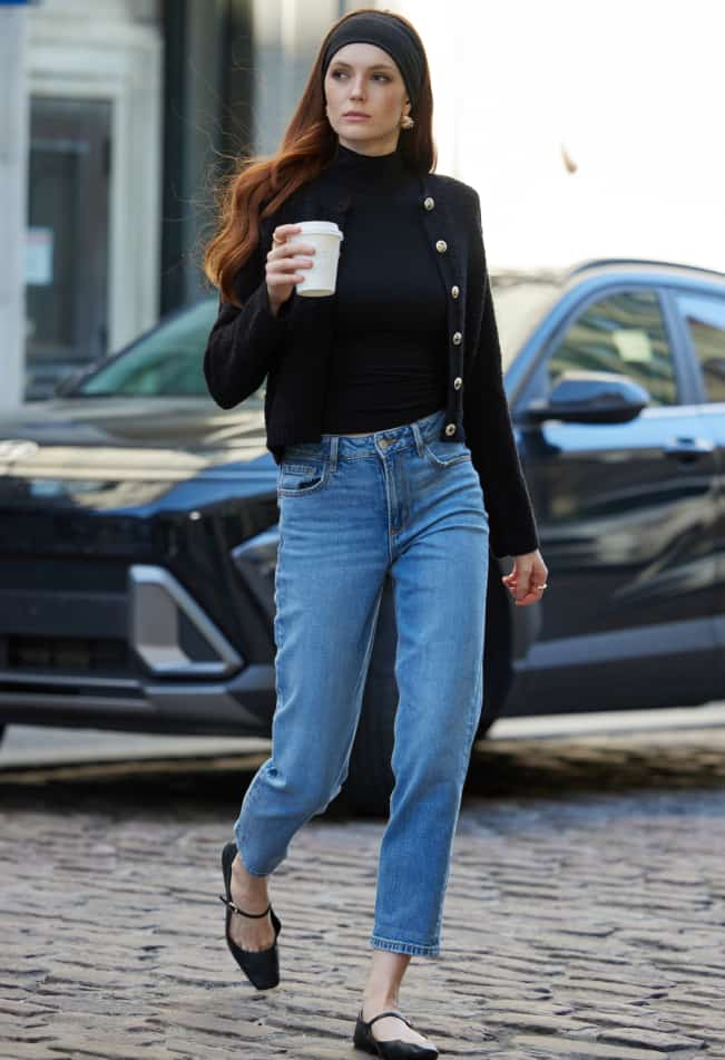 La mannequin porte un bandeau noir et un cardigan noir sur un haut à col roulé noir et un jean « mom » bleu.