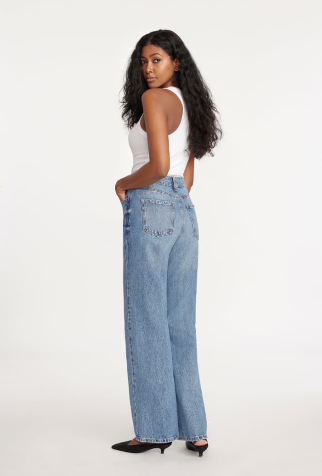 Model is wearing a white tank top and blue wide leg jeans.