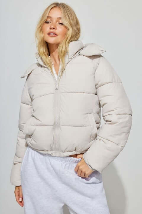 Model wears a beige puffer coat with grey sweatpants.