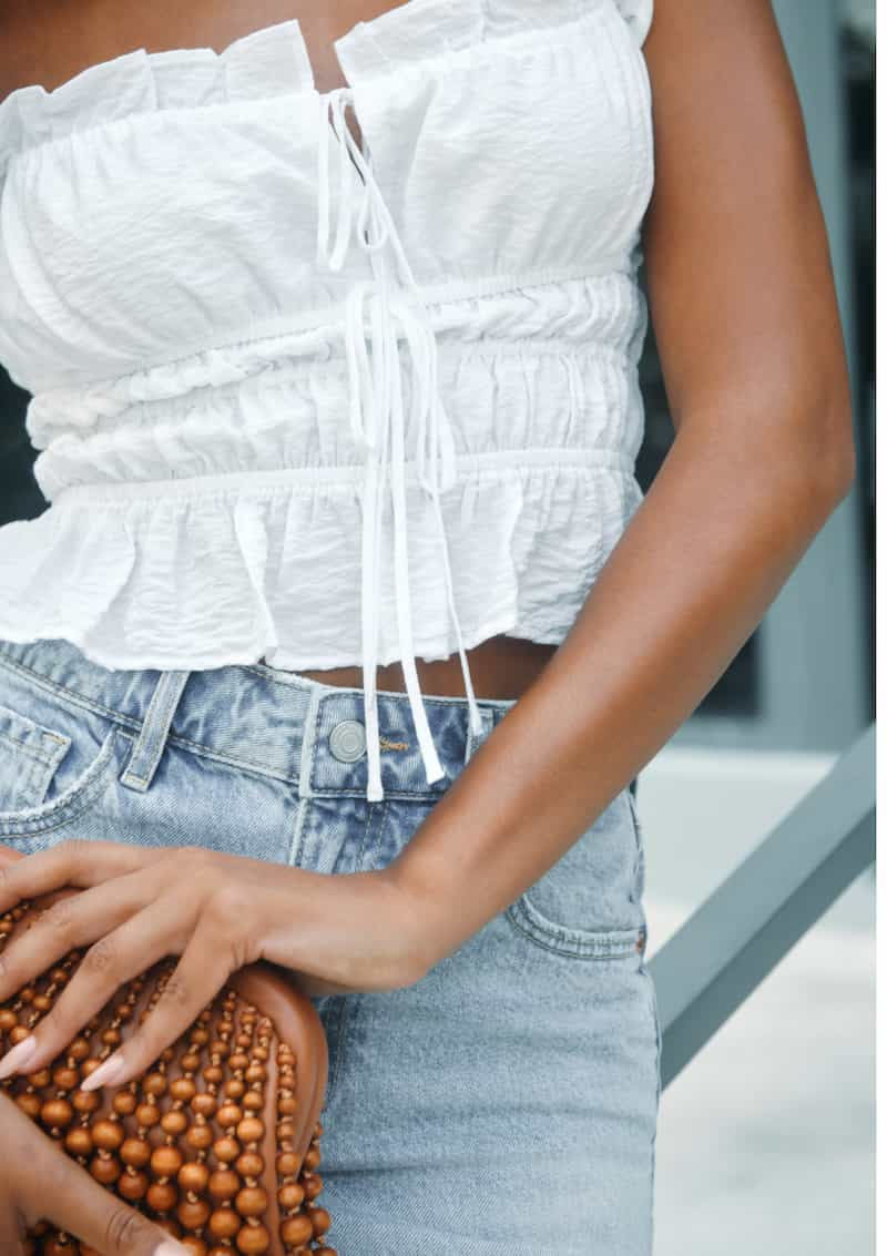 Model is wearing a white Maria shirred bow cami with a denim mini skirt.