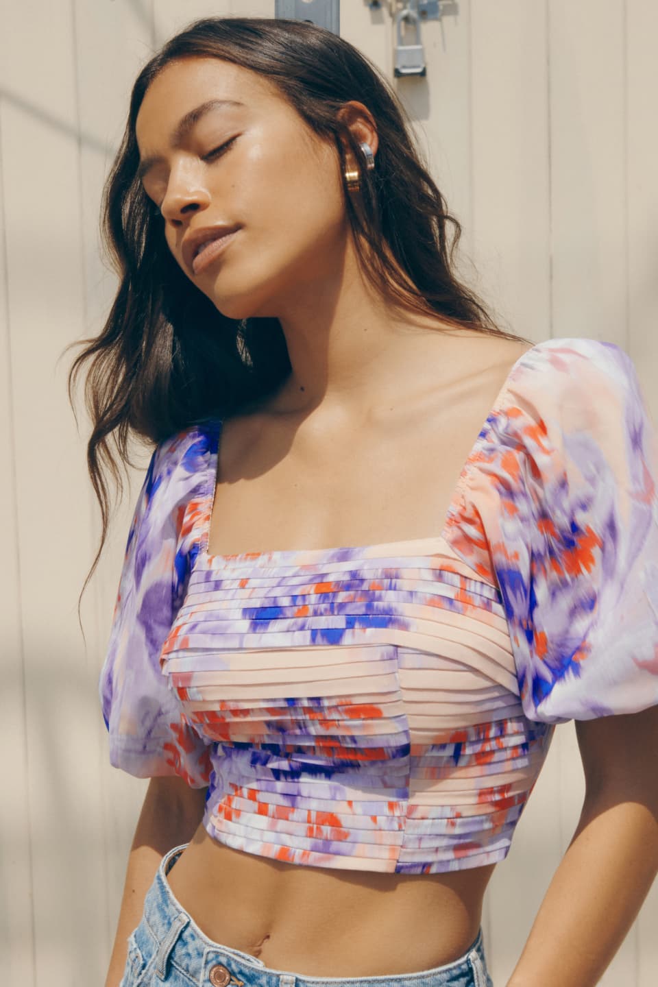 A model wears a cropped purple and pink printed top with short puff sleeves.