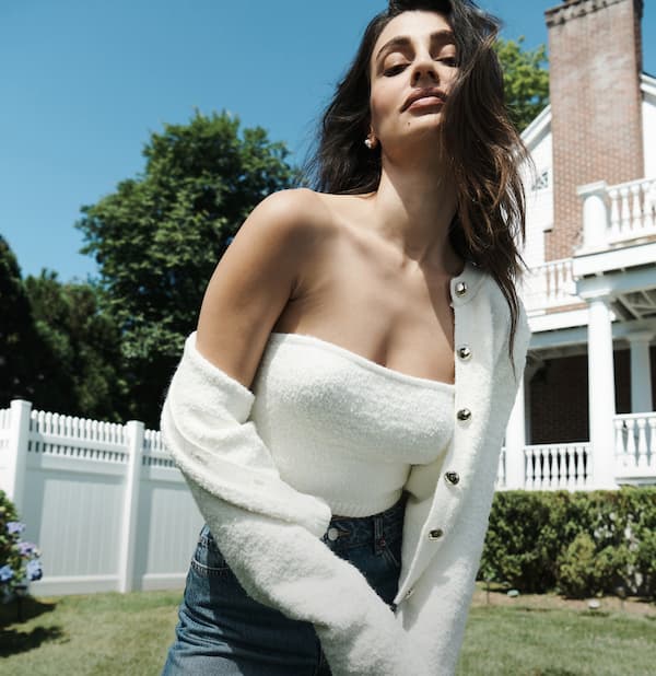 Model is wearing a white cardigan over a white tank top and blue jeans.