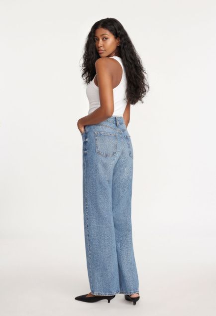 Model is wearing a white tank top and blue wide leg jeans.