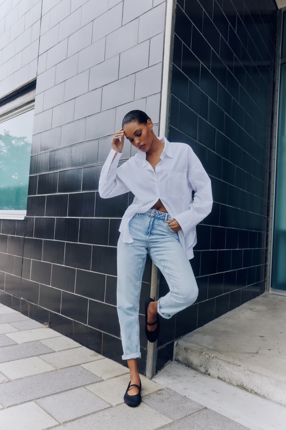 A model wears light blue slim jeans with a white button down shirt.