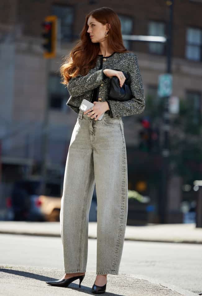 La mannequin porte une veste en tweed noir et un jean jambe ballon gris.