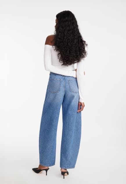 Model is wearing a white scoop neck tank top and blue barrel leg jeans.