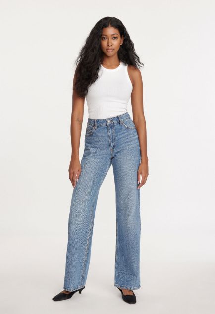 Model is wearing a white tank top and blue wide leg jeans.