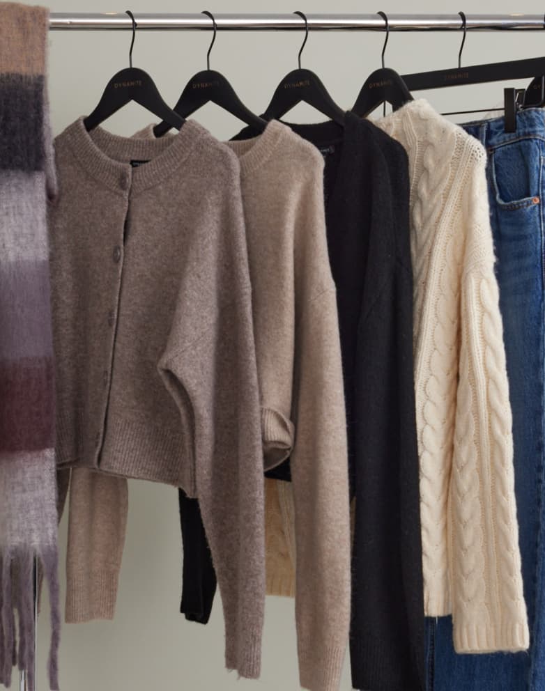 Beige, brown, and black sweaters hang from a clothing rack.