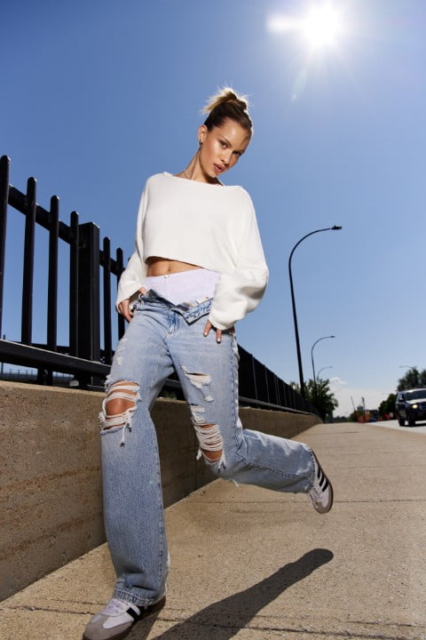 Model wears a white cropped sweater and distressed baggy jeans.