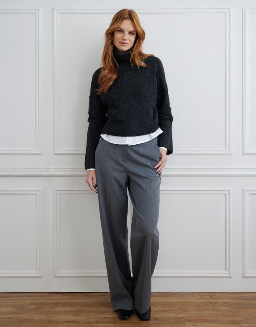 Model is wearing a black turtleneck over a white shirt and grey pants.