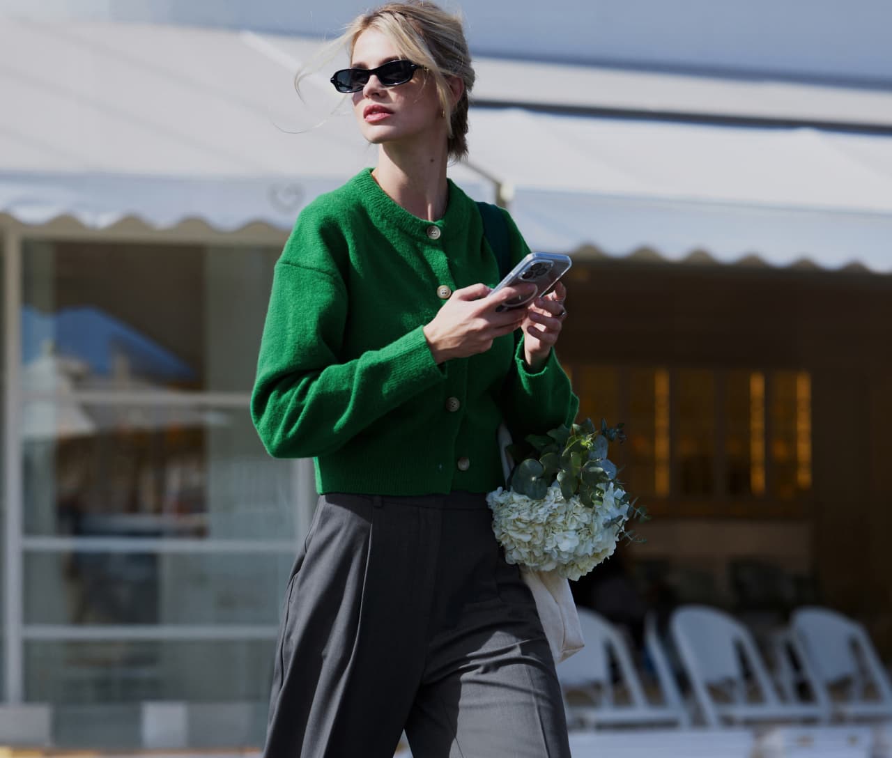 Model is wearing a green cardigan with grey pleated pants and black rectangular sunglasses.