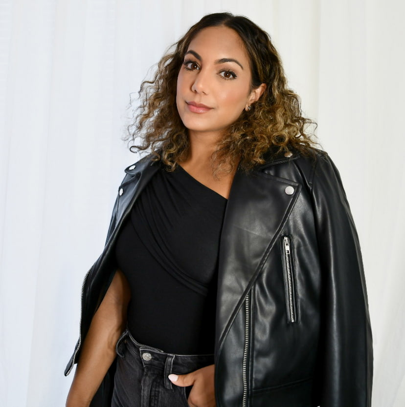 An influencer wears a black one-shoulder top with black jeans and a black faux leather moto jacket.