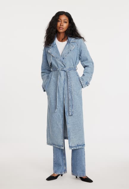 Model is wearing a blue denim trench coat over a white T-shirt and blue jeans.