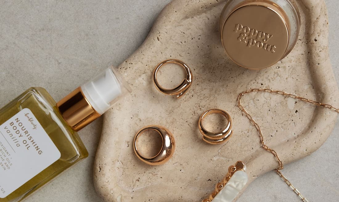 An image of gold rings, a gold necklace, and a beige barrette in a ceramic tray.