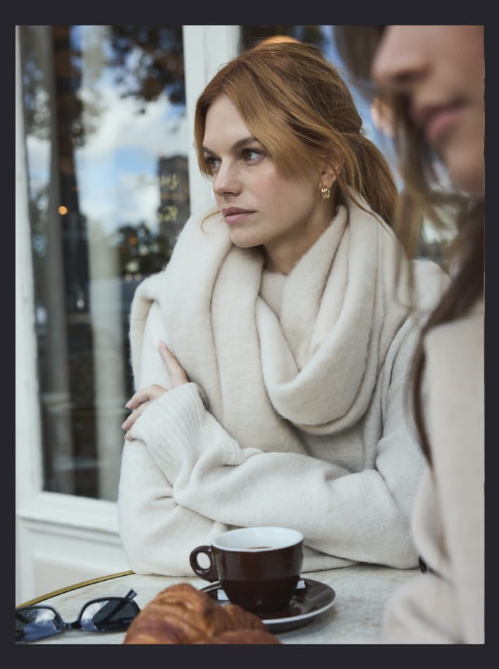 Model is wearing a beige scarf with a white sweater.