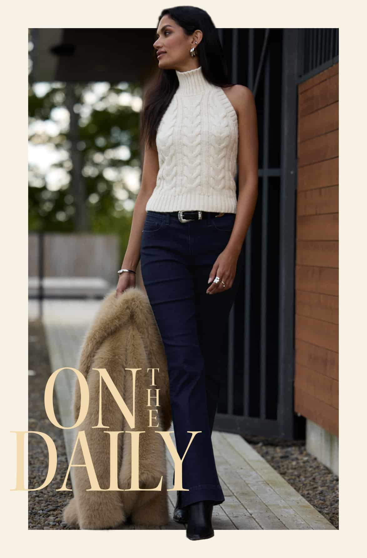 Model is wearing a white halter vest and blue jeans with a beige faux fur jacket.