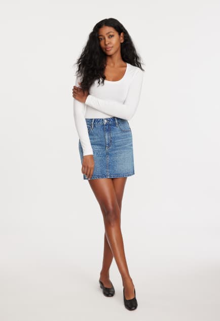 Model is wearing a white long sleeve shirt and a blue denim maxi skirt.