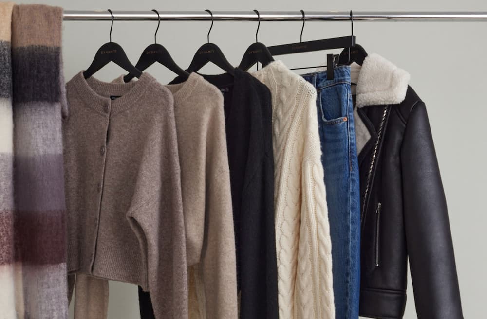 A collection of cardigans, sweaters, jeans, and jackets hang on a clothing rack.