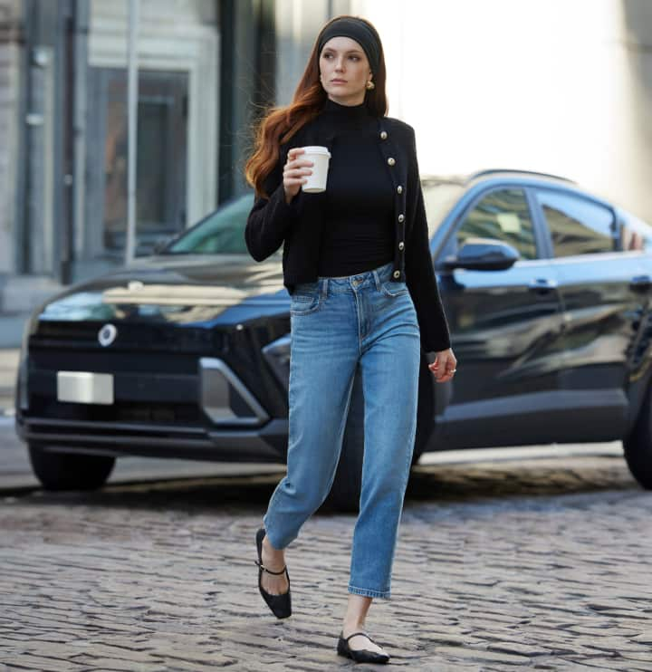 Model is wearing a black cardigan over a black turtleneck and blue jeans.