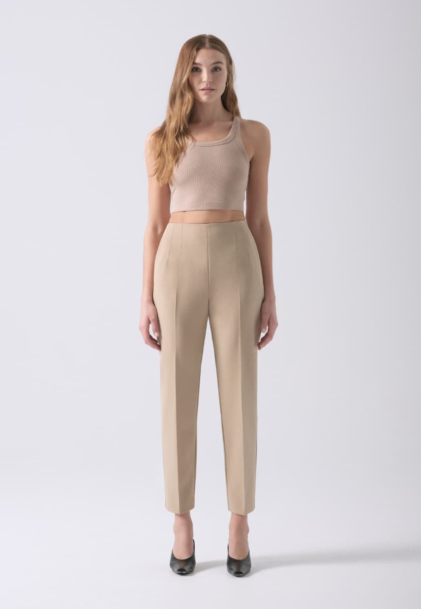 A model wears beige slim leg pants with a beige tank top.