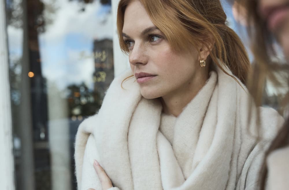 Model wears off-white scarf and a sweater at a cafe.