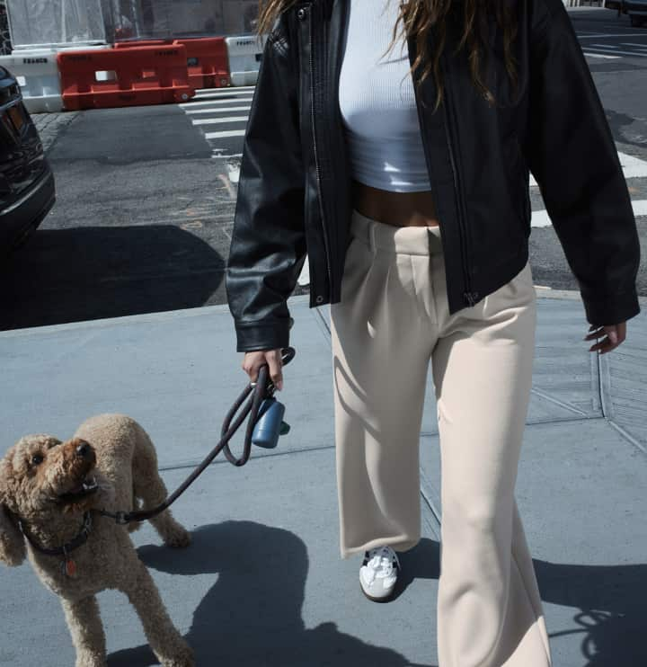 Model is wearing a black faux leather jacket over a white t-shirt and beige pants.