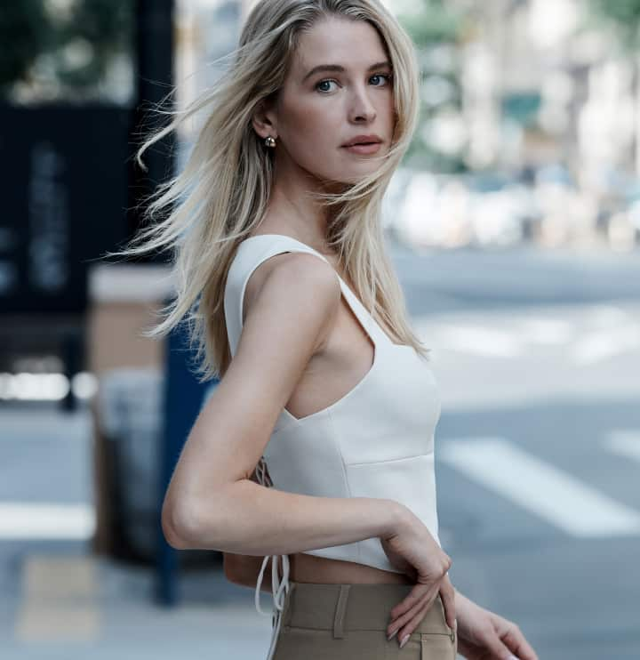 Model is wearing a white tank top and brown pants.